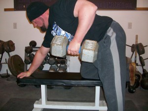 A man in a gym holding Dumbbell and leg on a bench while exercising.